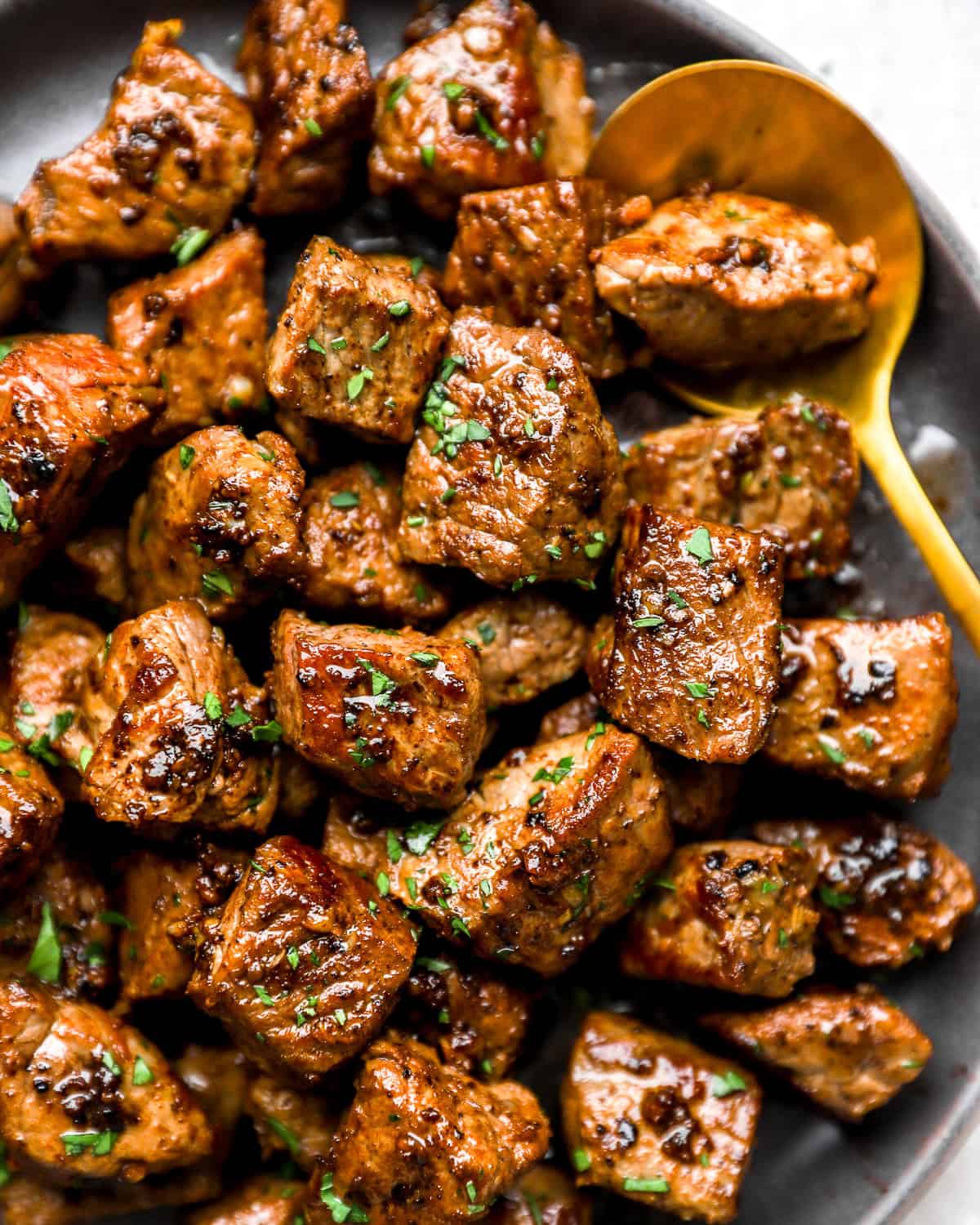 Garlic butter steak bites with browned edges and fresh parsley in a bowl.