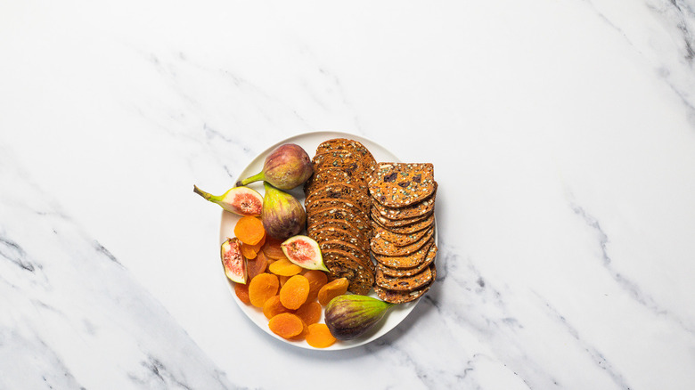 Dried apricots, fresh figs, and crackers on a plate.