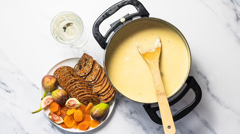 Wooden spoon in a bleu cheese and honey fondue, alongside dried apricots, fresh figs, and crackers on a plate.