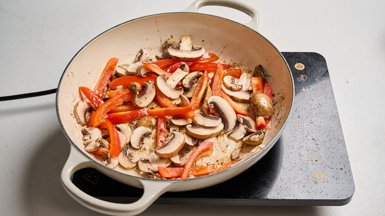 cooking red bell peppers and mushrooms in a skillet