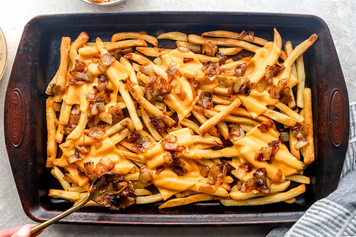 Close-up of animal style fries being drizzled with creamy sauce and topped with caramelized onions