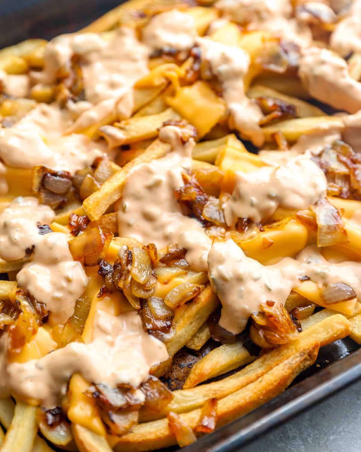 Animal style fries topped with melted American cheese, caramelized onions, and creamy sauce on a sheet pan