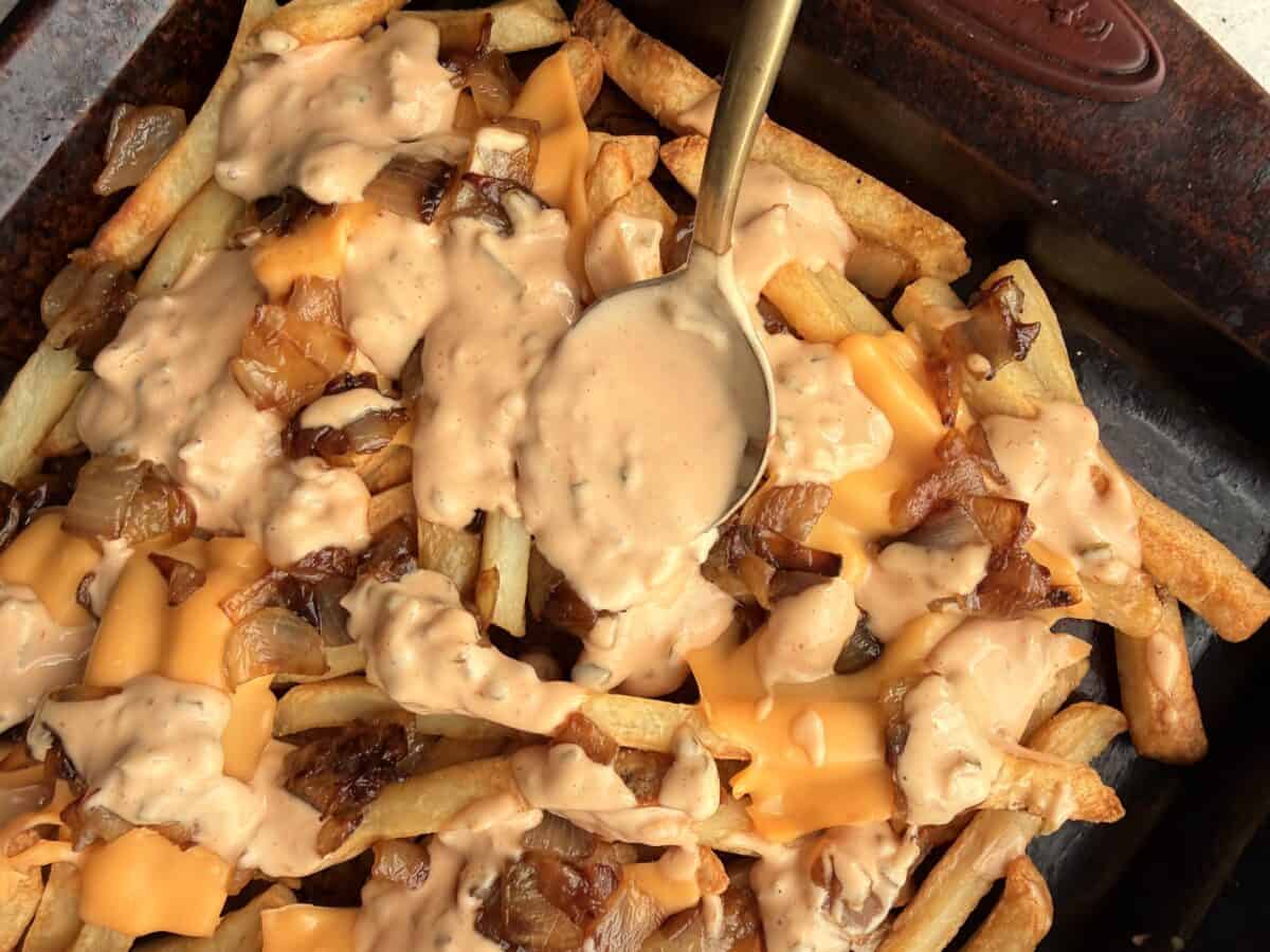 Close-up of animal style fries with melted American cheese, caramelized onions, and creamy sauce being spooned over the top