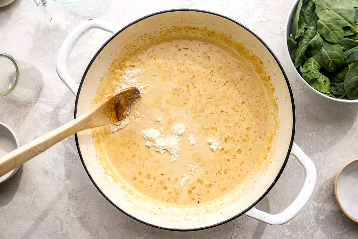 Cream sauce simmering in a skillet with visible onions and seasoning