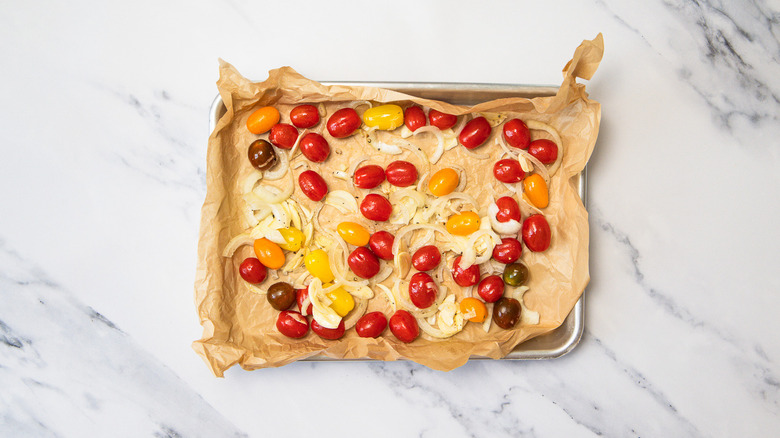 Tomatoes and onion on baking sheet.