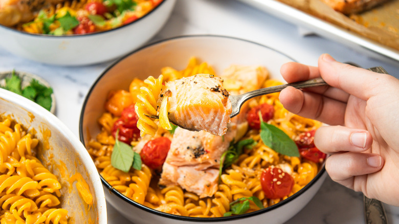One hand lifting a fork with cooked salmon over bowl.