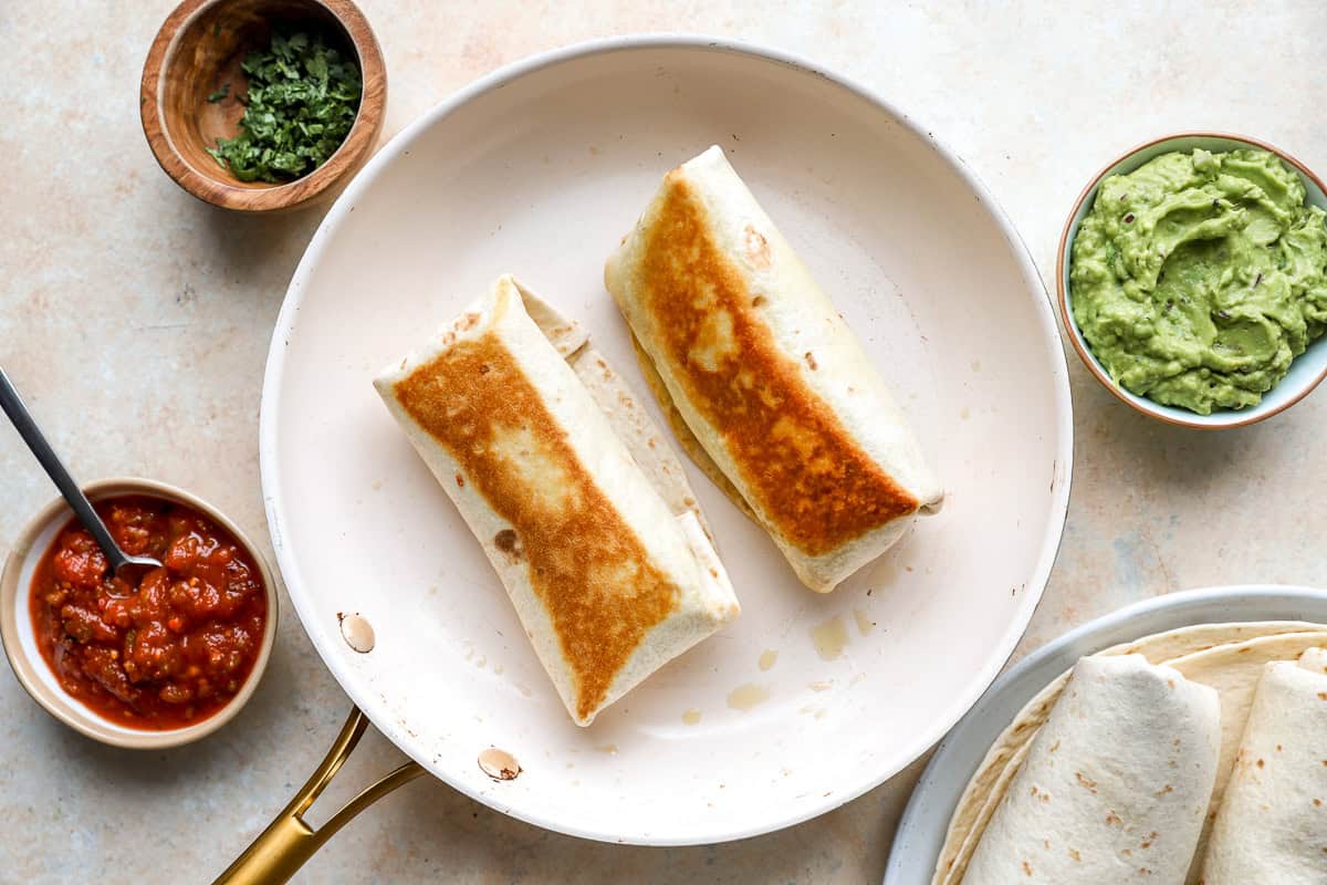 Bean and cheese burritos crisping in a skillet until golden brown.
