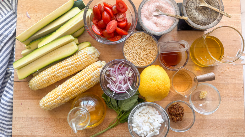 Summer orzo pasta salad ingredients on wooden board