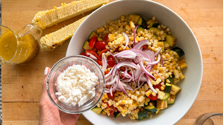 hand adding feta to bowl of pasta salad