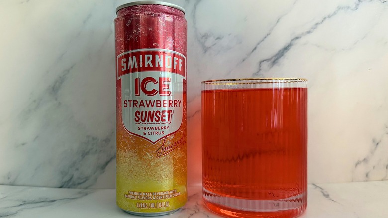 Can of Strawberry Sunset Smirnoff Ice next to glass of Smirnoff Ice on marble surface