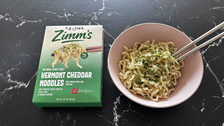 A-Sha/Zimm's Vermont cheddar noodles box next to prepared noodles in bowl
