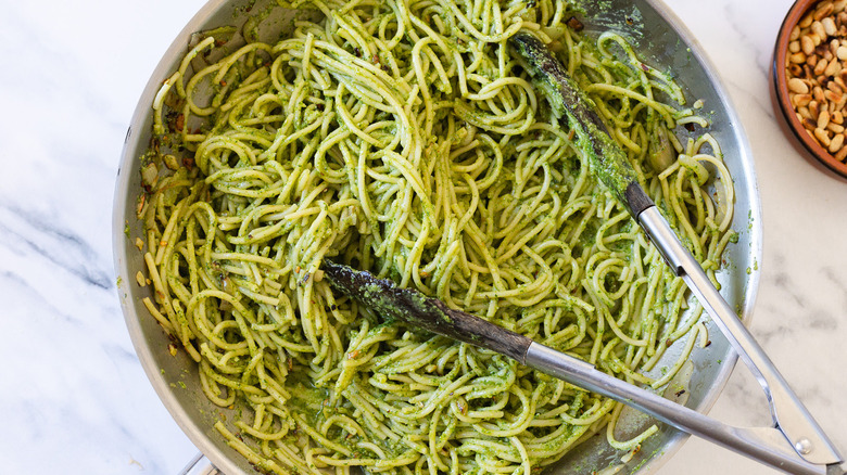 Pesto pasta with tongs in a pan.