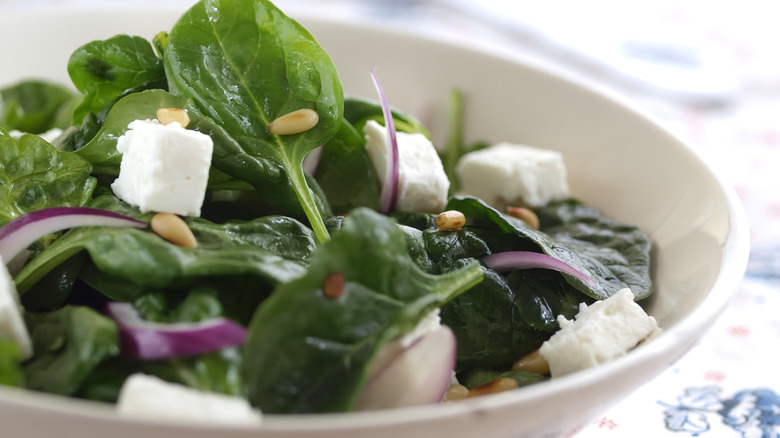 Close up on a spinach salad with feta cheese, red onions, and pine nuts