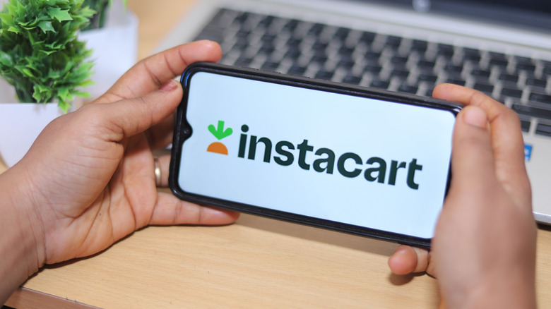 Hands holding smartphone horizontally with screen displaying Instacart logo