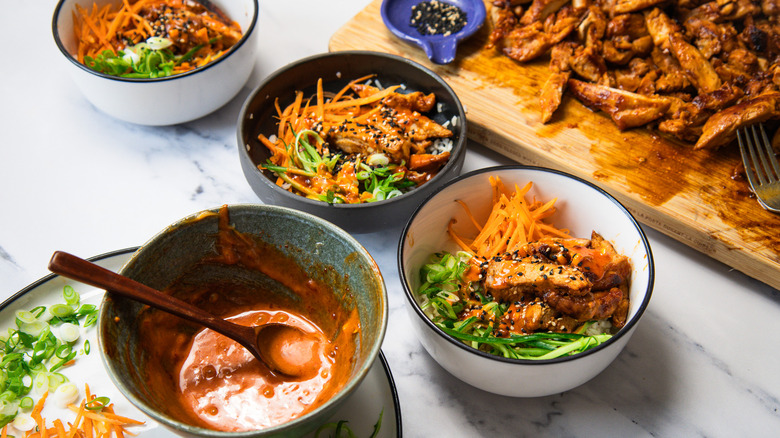 Assembling three Korean BBQ chicken rice bowls.