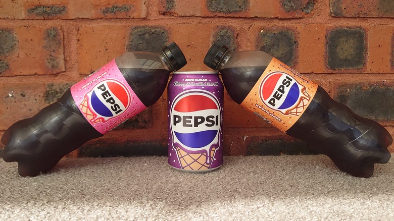 Two bottles of Pepsi balanced on a can in front of the brick background