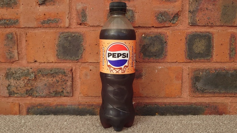 A close up shot of a Pepsi Salted Caramel bottle on a blanket and a red brick background