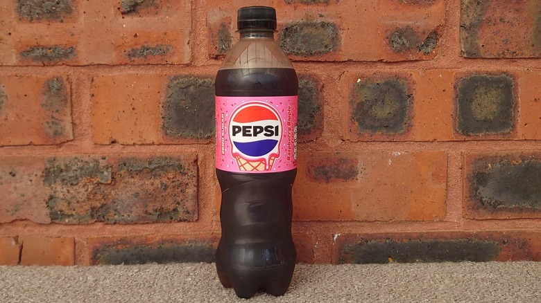 A close up shot of a Pepsi Raspberry Ripple bottle on a blanket and a red brick background