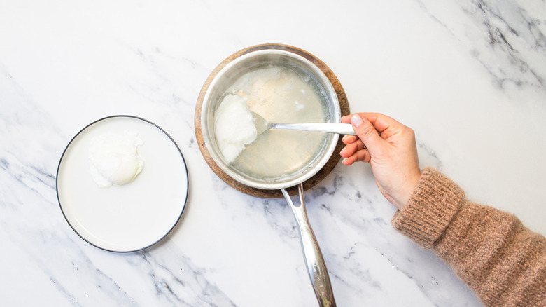 Lifting a poached egg from saucepan.