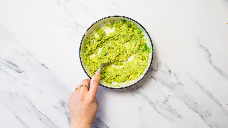 Mashing avocados with fork in bowl.