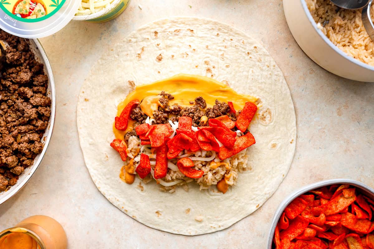 Burrito tortilla layered with nacho cheese, taco beef, rice, shredded cheese, chipotle sauce, and Flamin’ Hot Fritos before rolling.
