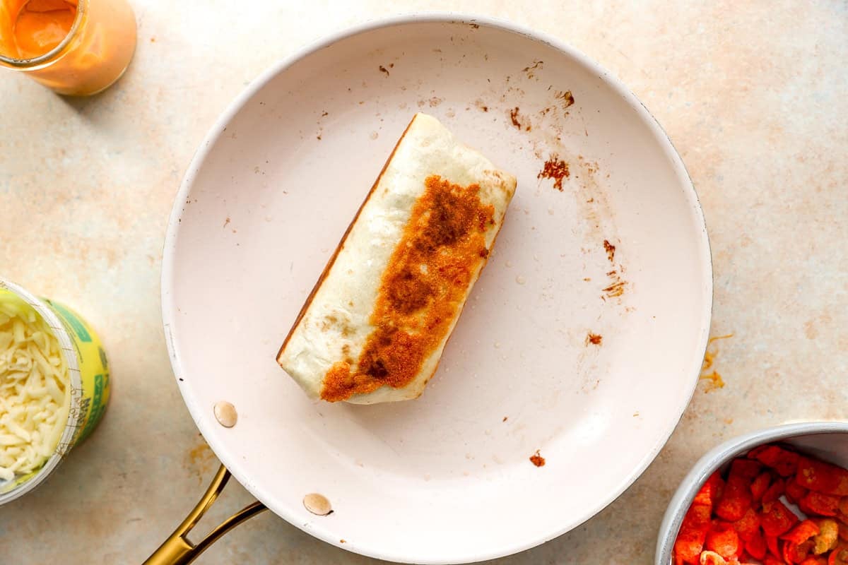 Crispy melted cheese crust forming underneath a grilled cheese burrito in a skillet.