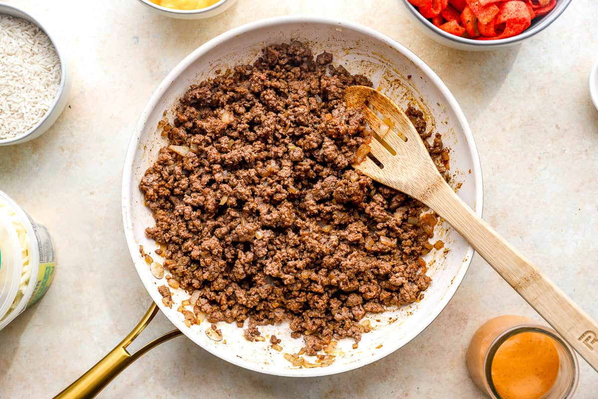 Seasoned ground beef cooking in a skillet with onions for Flamin’ Hot grilled cheese burritos.
