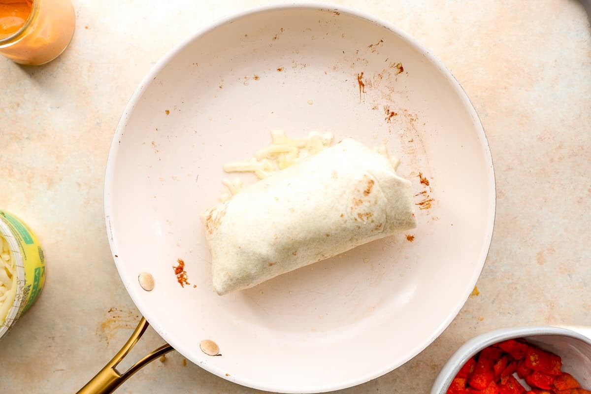 Burrito placed seam-side down onto melted cheese in a skillet before crisping.