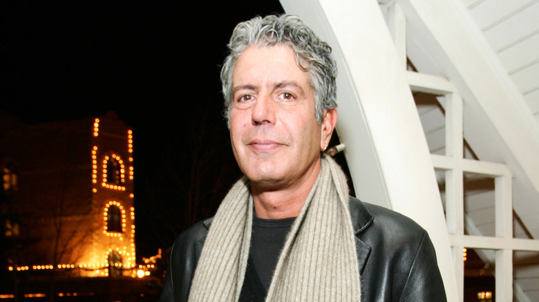 Anthony Bourdain standing outside with an illuminated building in the background