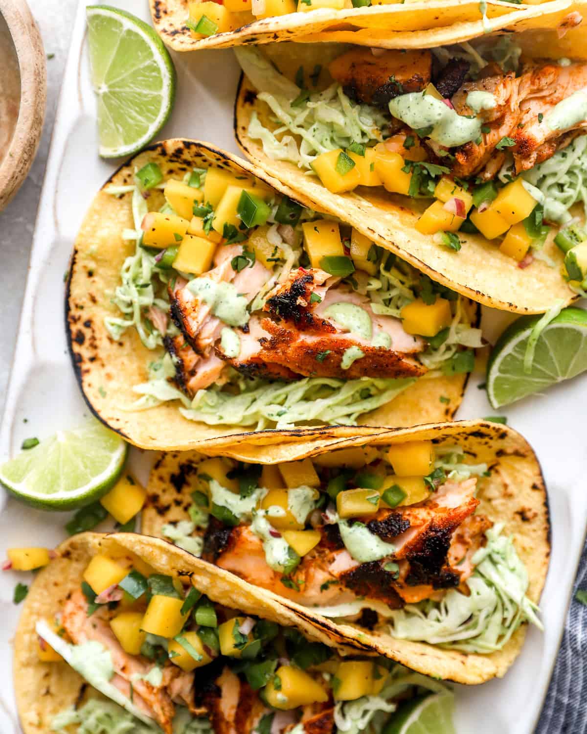 Salmon tacos topped with mango salsa and cilantro lime slaw on charred corn tortillas with fresh lime wedges.