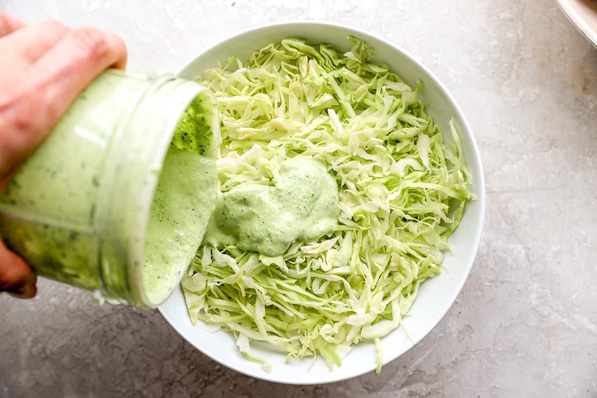 Creamy cilantro lime dressing being poured over shredded cabbage for homemade taco slaw.