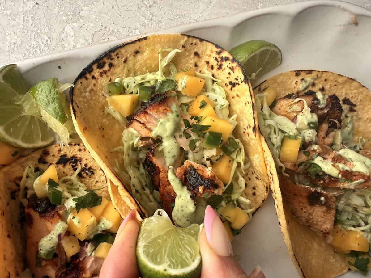 woman squeezing lime juice on finished salmon tacos 