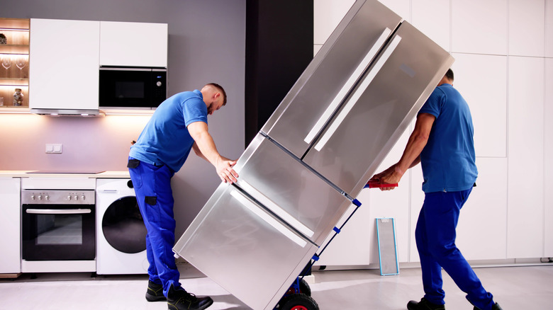 Two delivery workers roll fridge into kitchen for installation