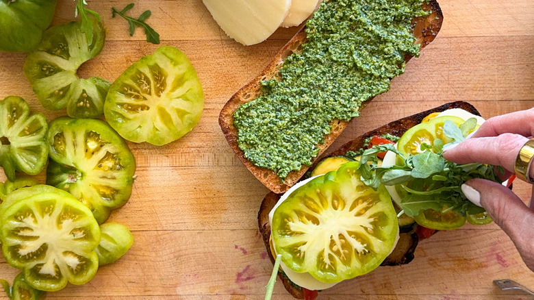 hand adding arugula to sandwich