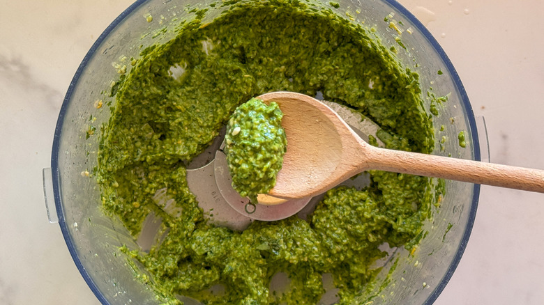 spoon mixing pesto in food processor
