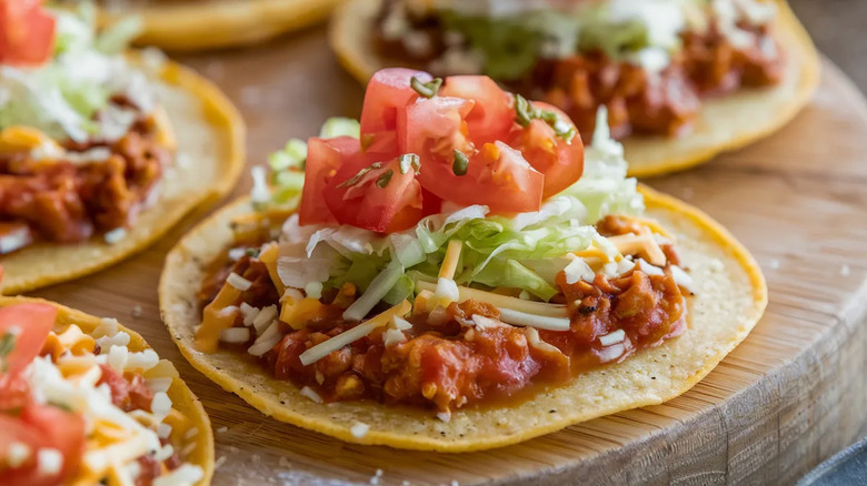 A tostada topped with seasoned meat, cheese, lettuce, and tomato