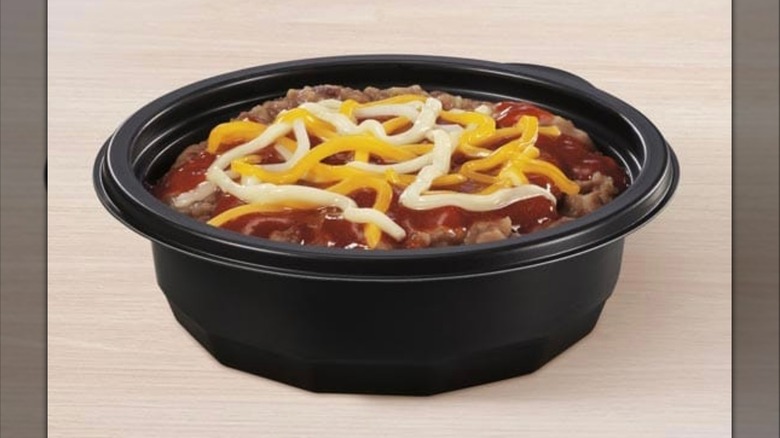 A black bowl of refried pinto beans topped with red sauce and cheese