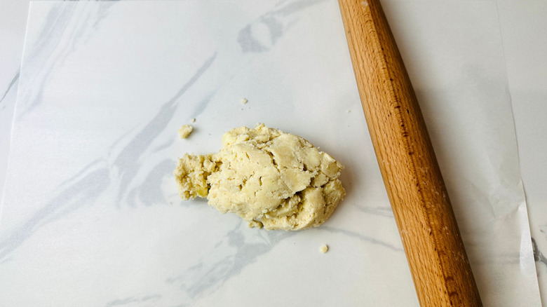 Pie crust dough next to rolling pin on parchment paper