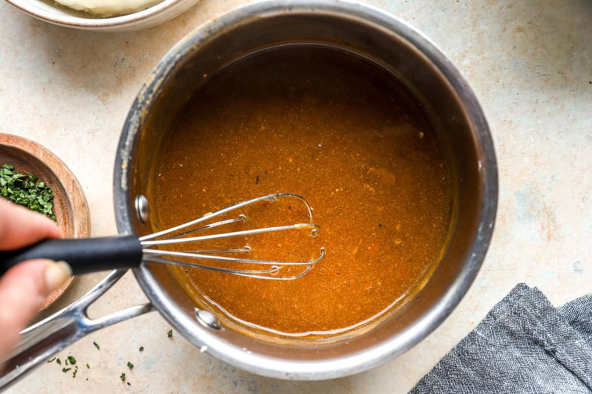 Homemade pork gravy whisking in a saucepan made from roasted pork pan drippings.
