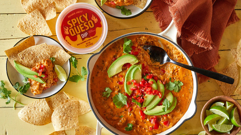 A package of Trader Joe's Spicy Queso Dip next to a dish of dip and plates of chips