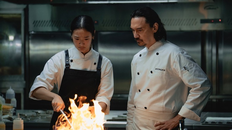 Aoy nervous prepares a dish in a flaming wok while Chef Paul watches