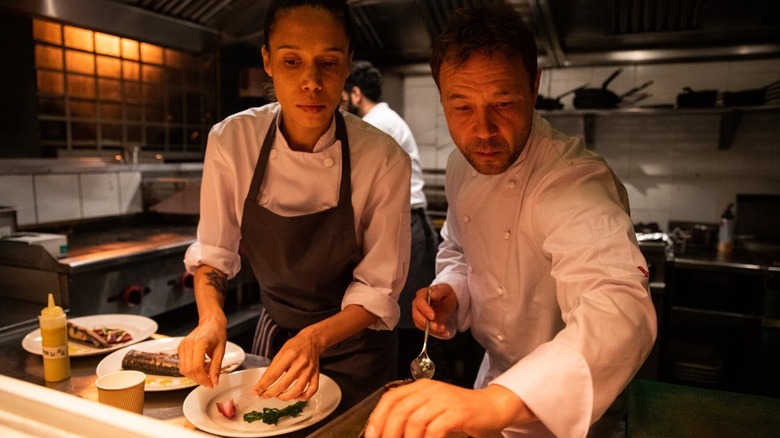 A still from &quotBoiling Point&quot depicting Andy and Carly in chef's whites preparing a dish