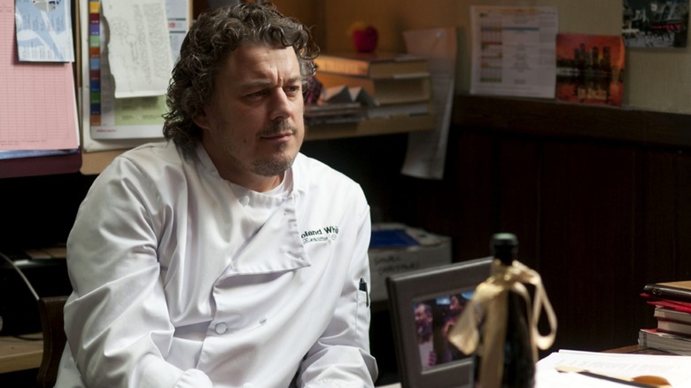 Chef Roland White smirking while sitting in his office in a still from 