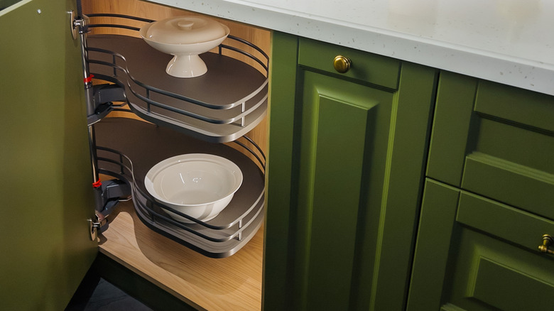 An open olive green cabinet with white dishes inside