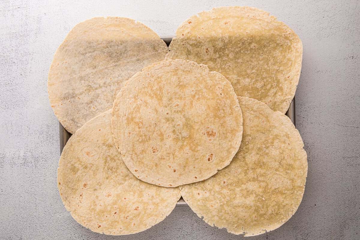 Overhead view of flour tortillas arranged and overlapping in a sheet pan to form the base of a sheet pan crunchwrap.