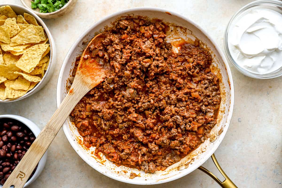 Ground beef taco filling cooking in a skillet with onions, taco seasoning, and tomato sauce