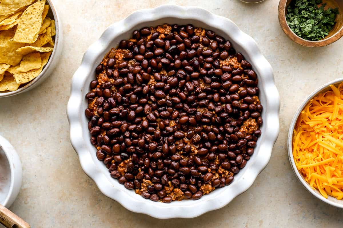 Layer of black beans spread over seasoned taco meat in a pie dish