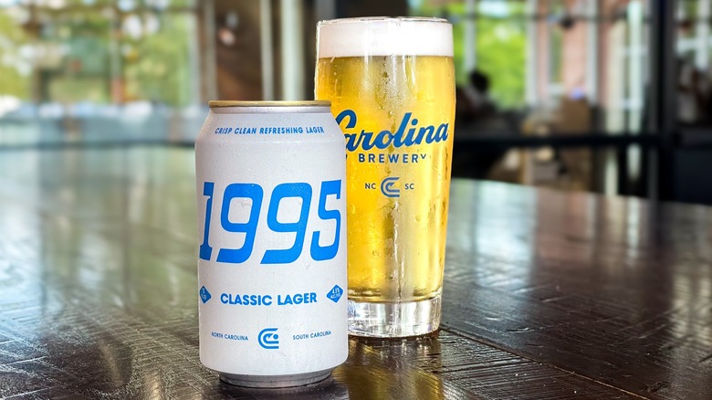 Can of Carolina Brewery 1995 Classic Lager next to pint glass of lager on wooden table