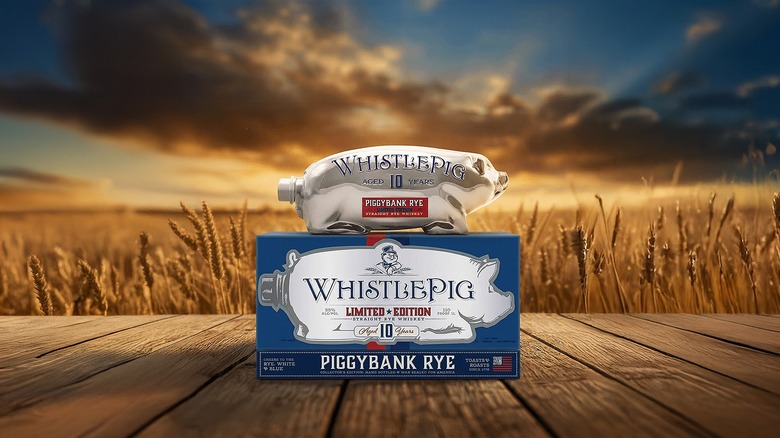 Pig-shaped bottle of whiskey on top of WhistlePig Piggy Bank Rye box, with wheat field and sky in background