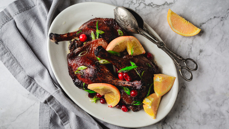 Roasted duck legs on plate with fresh cranberries and orange slices
